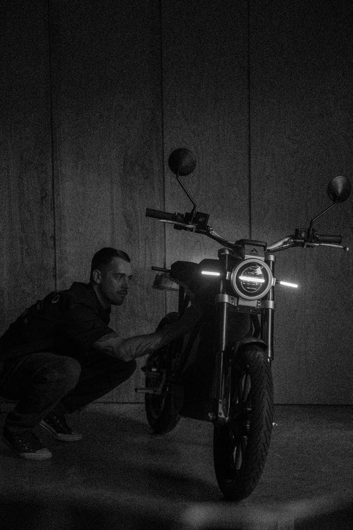 Designer crouched next to a LAND electric motorcycle in a darkened studio